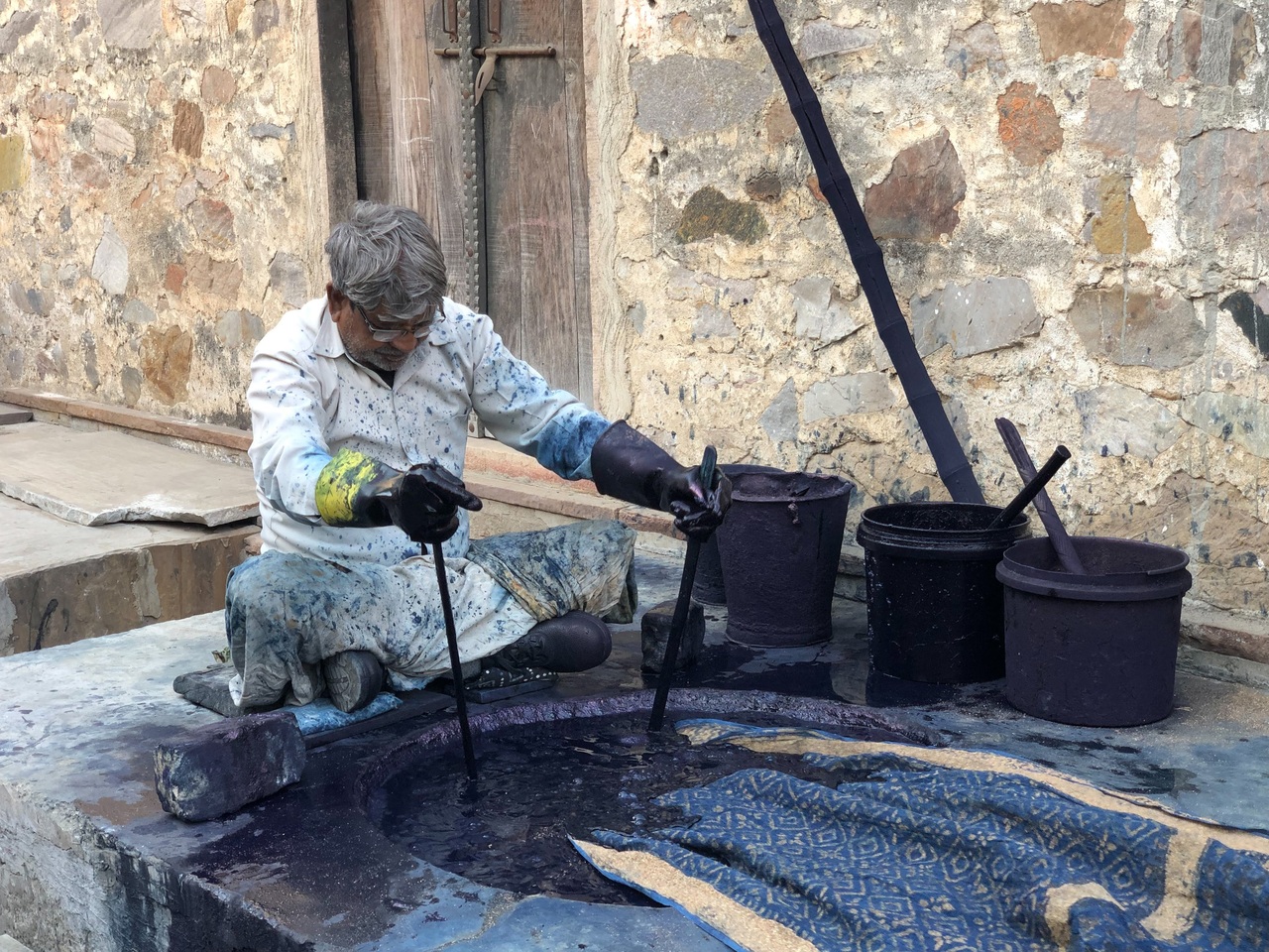The local indigo dyers sits beside his under ground indigo vat and dips a piece of large block printed fabric.