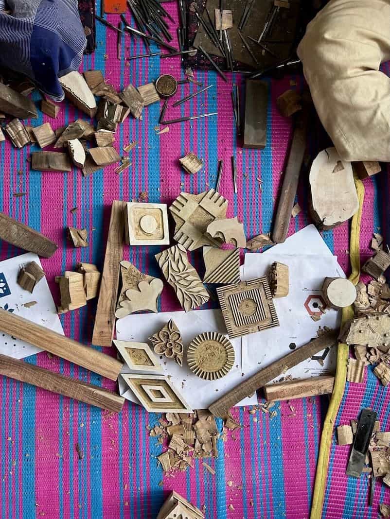 Various carved wooden blocks, chisels, and wood shavings scattered on a vibrant striped mat during a block carving workshop.