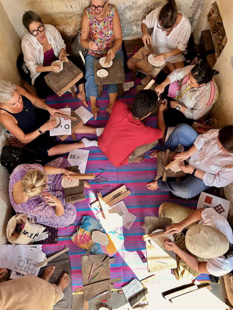 Group of participants sitting in a circle on the floor, actively engaged in carving wooden blocks during a hands-on workshop.