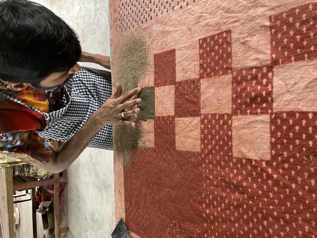 A man applying Dabu, a mud resist material to the block printed piece of fabric.