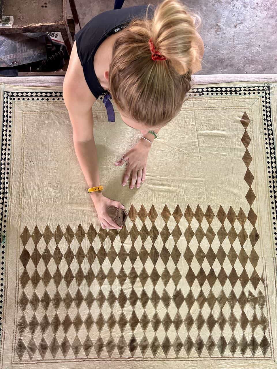 Participants at a long table engaged in hand block printing, stamping colorful designs onto white fabric using traditional wooden blocks.