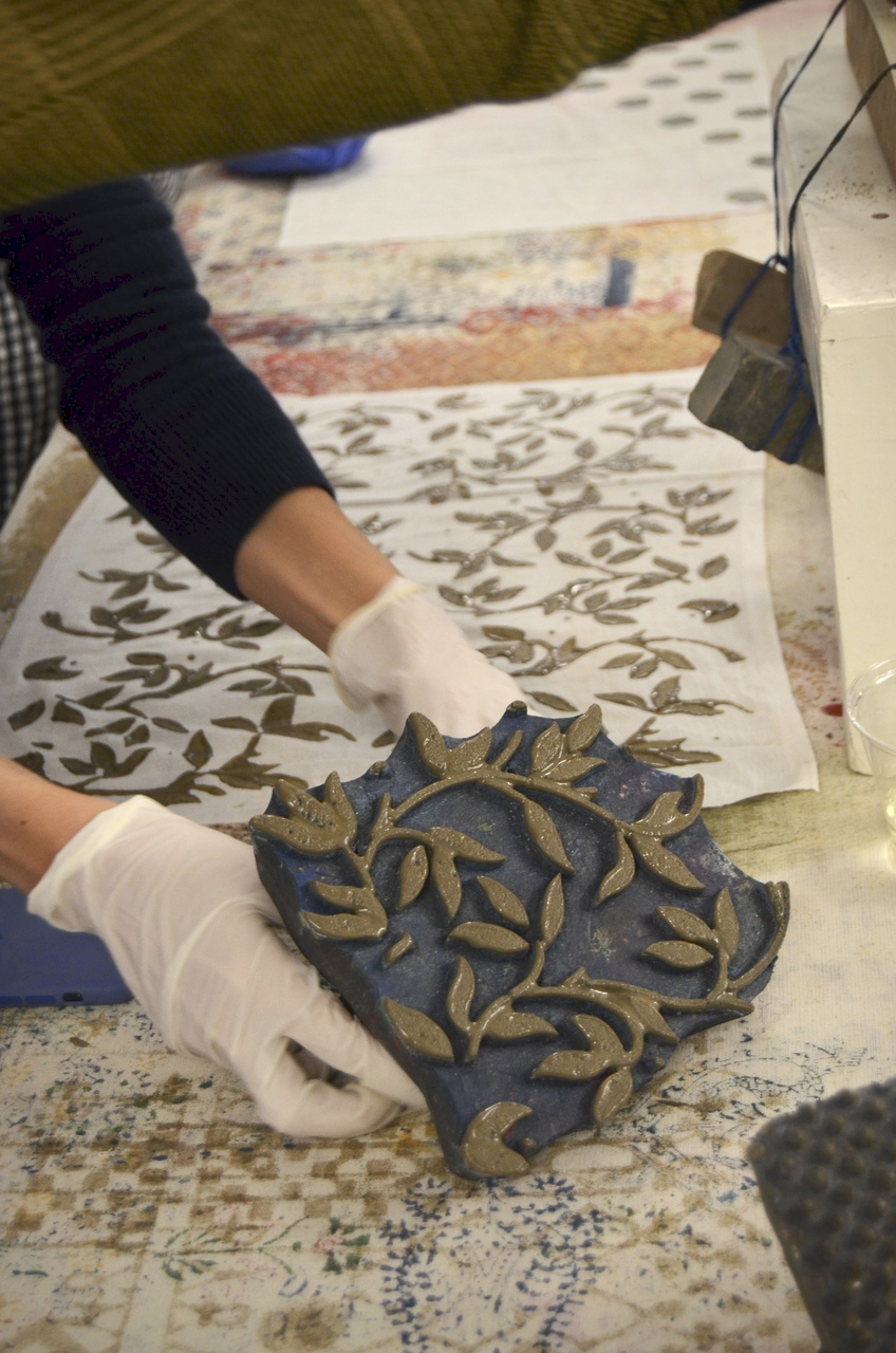 A picture showcasing a workshop attendee in the process of block printing a leafy pattern on a piece of cloth