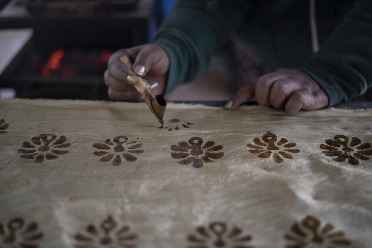 A man is creating wax based designs on the piece of fabric with the use of different wooden blocks, Tjanting, a pen-shaped tool.