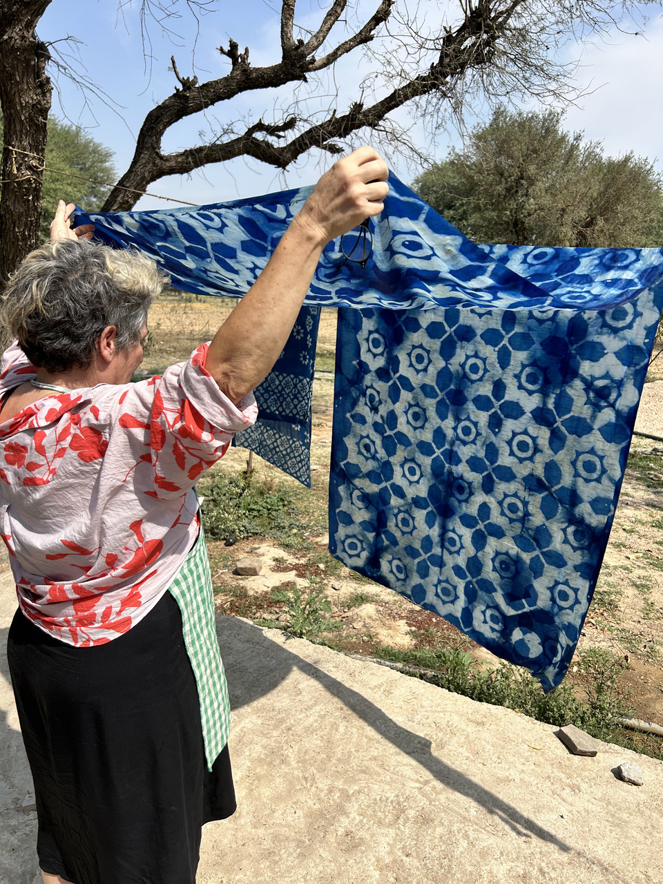 A women carefully observing the blue block printed mud resist dyed pattern drying in the outdoors.