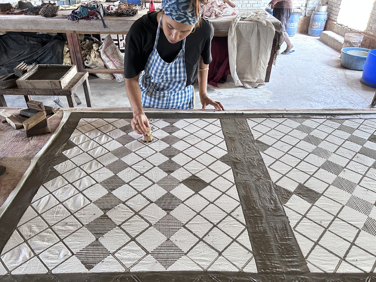 A women carefully trying to create a pattern using different blocks on the piece of fabric with the mud resist dye mixture.