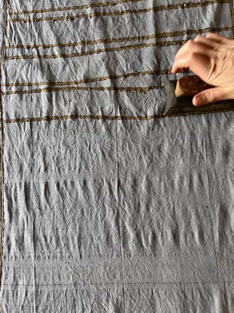 Close-up of a hand using a wooden block to print evenly spaced horizontal lines on fabric during a resist printing workshop.